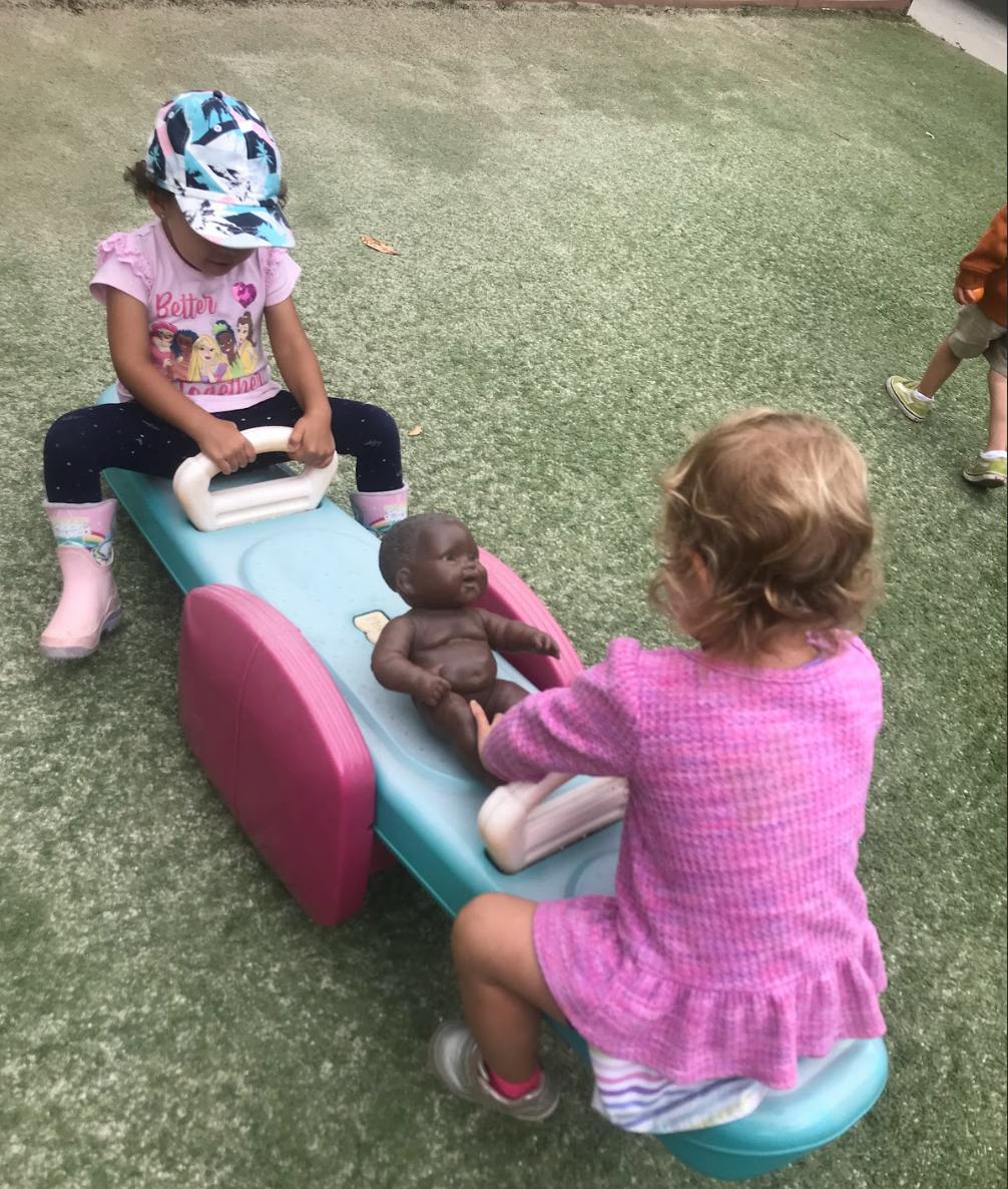 Two children playing on a seesaw with a doll