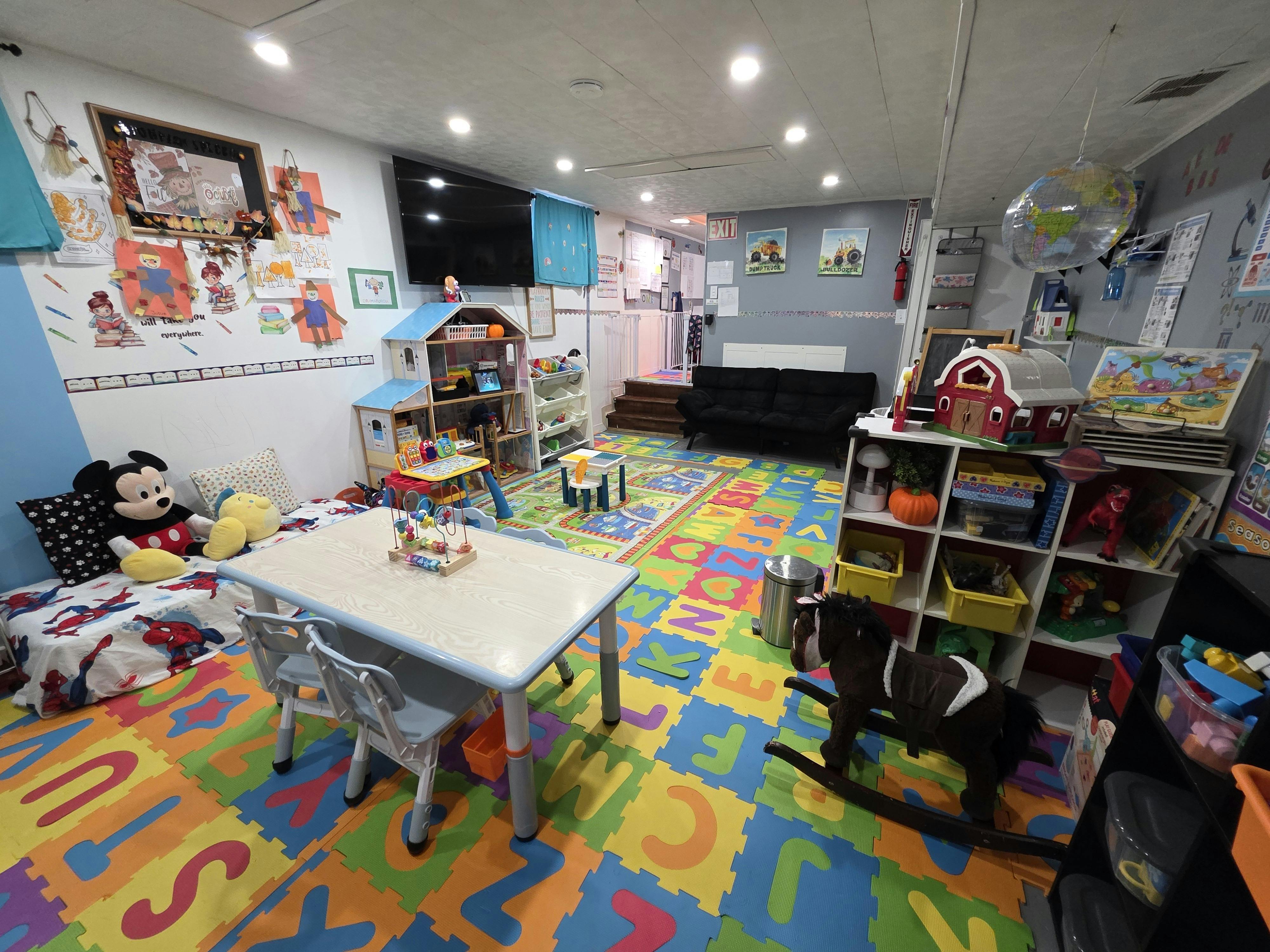 A colorful playroom with alphabet mat, toy horse, tables, and shelves of children's drawings