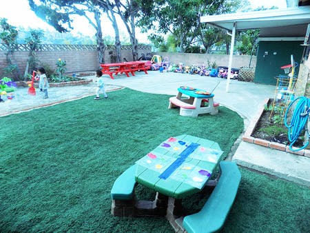 Two children playing in a backyard with artificial turf and a sandbox