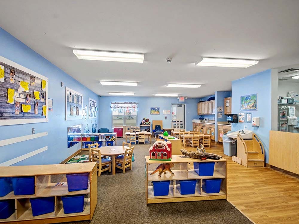 Classroom with light blue walls, small tables, and shelves with blue bins