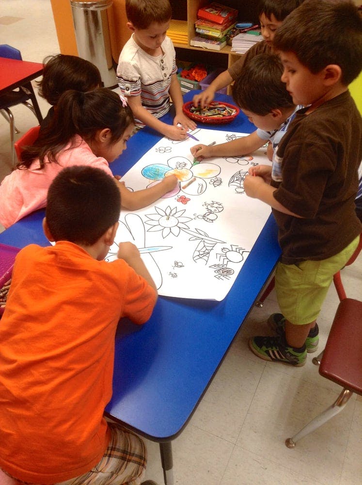 Children coloring a large drawing on a blue table