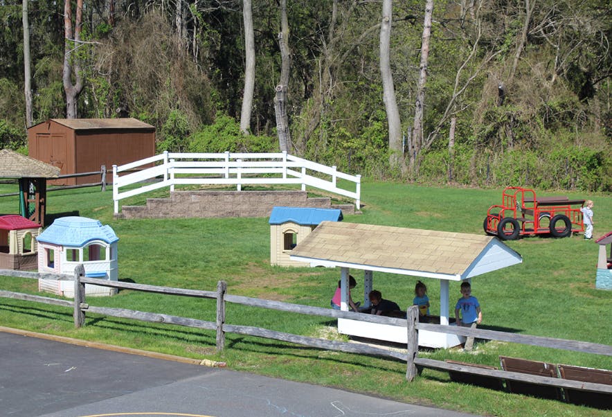 People under a shelter in a grassy area with playhouses and a wooden truck
