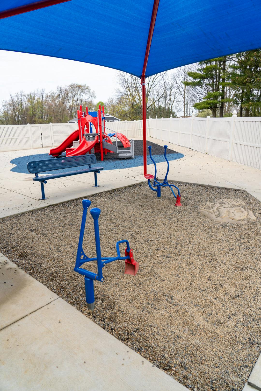 Playground with red slides, blue bench, and blue digging toys under a blue canopy