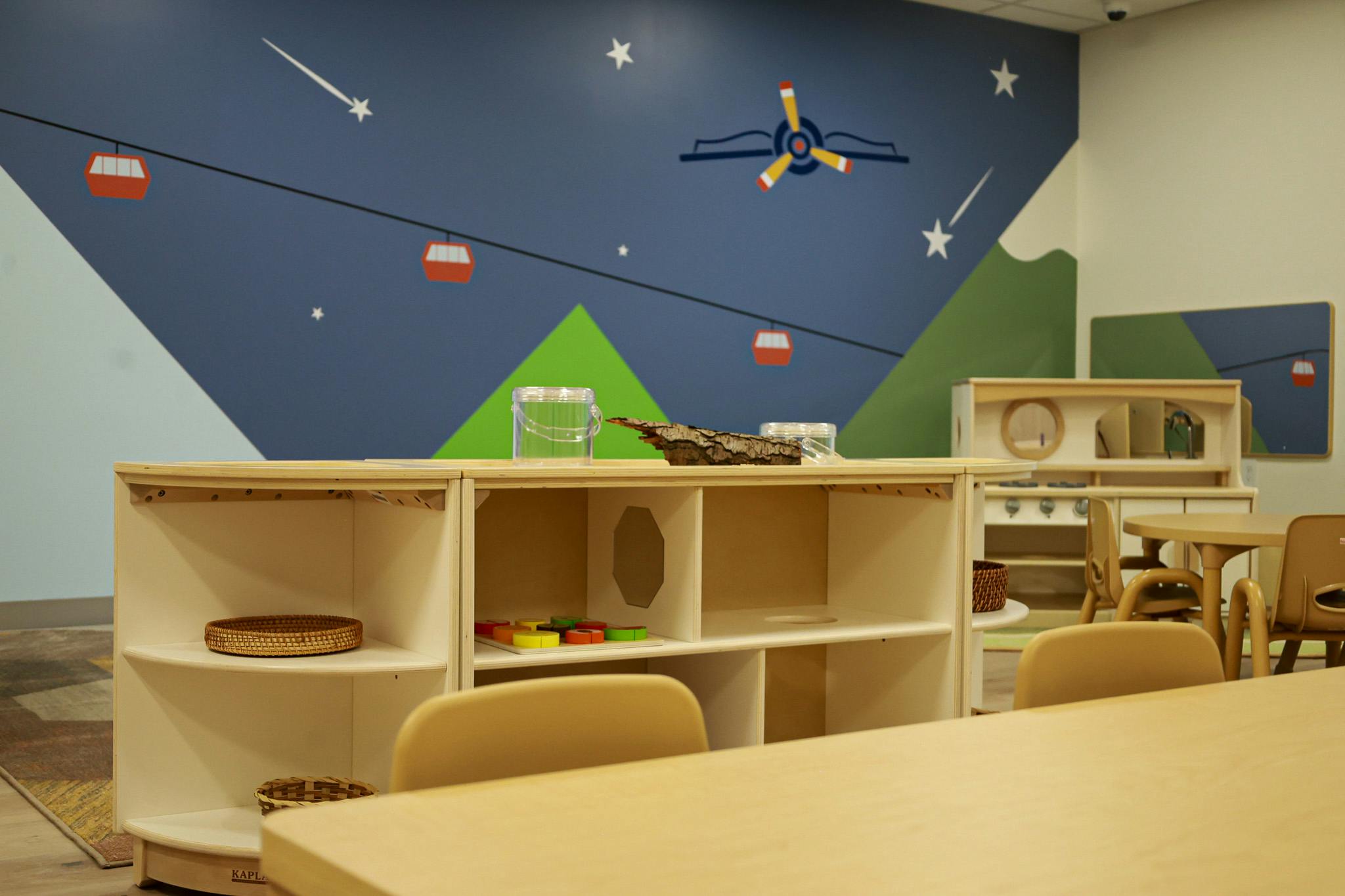 Wooden shelves and table in a childcare classroom with mountain wall mural