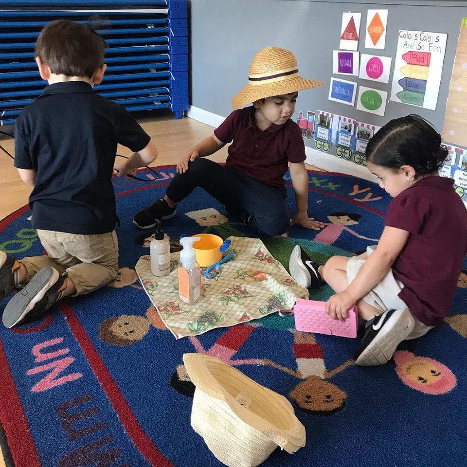 Three children playing on a rug with various items