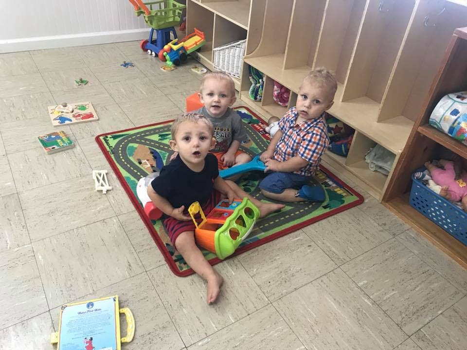 Three children sitting on a rug in a playroom
