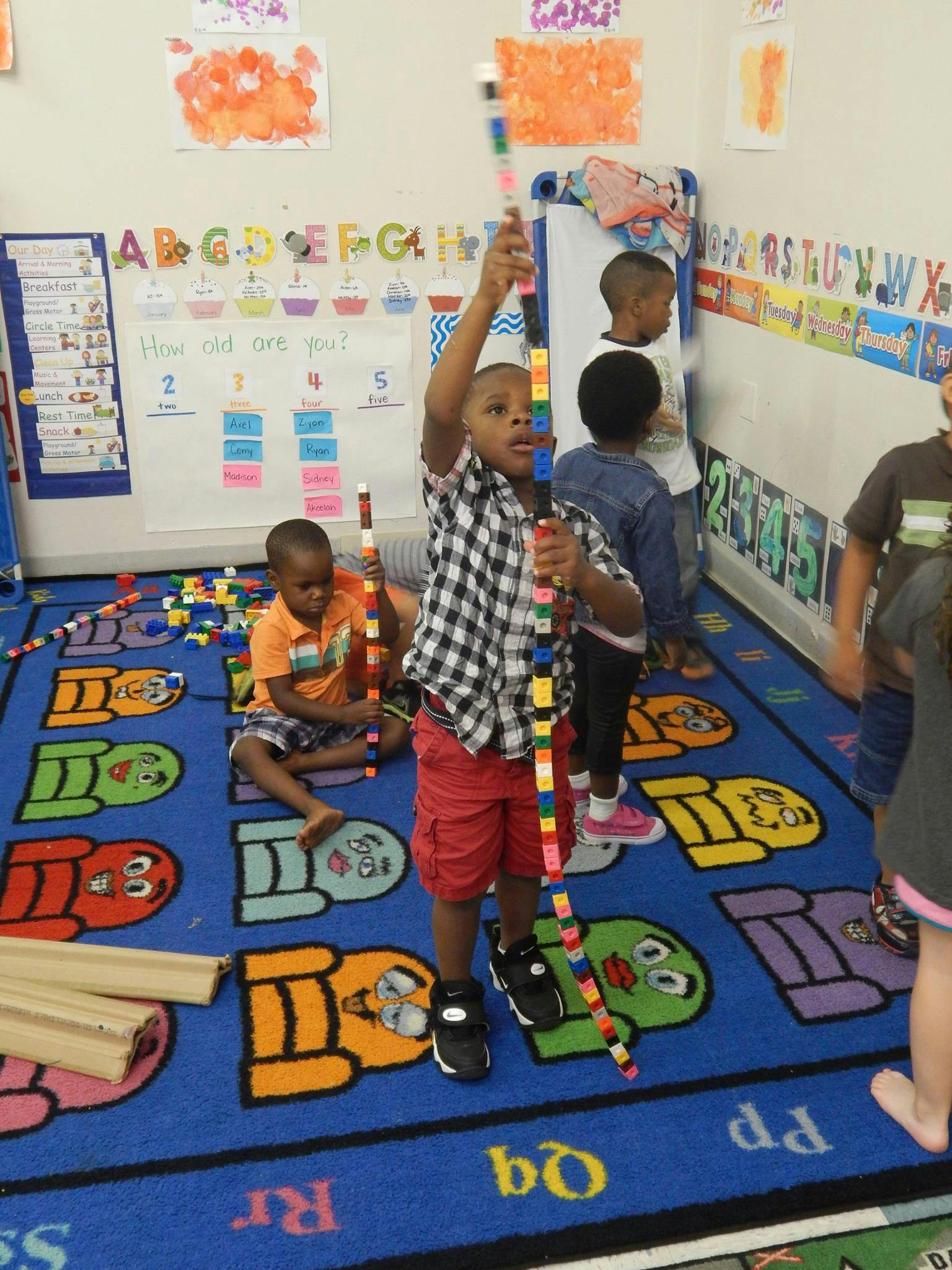 Child holding up a tall stack of colorful building blocks in a classroom
