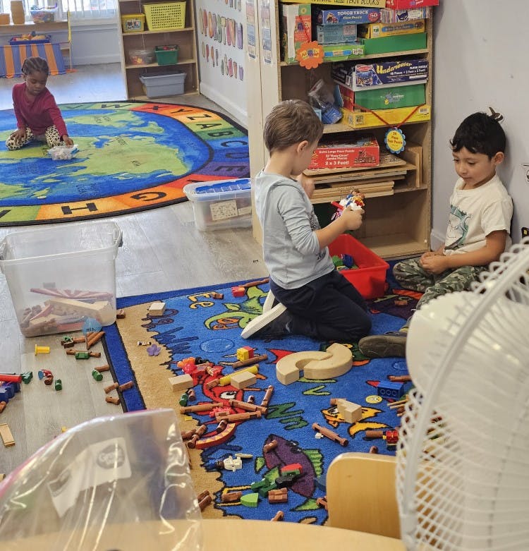 Three children playing with building blocks on rugs in a classroom