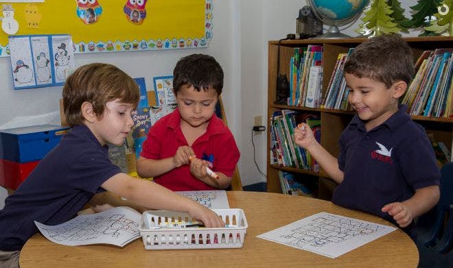 Three children coloring at a table in a classroom
