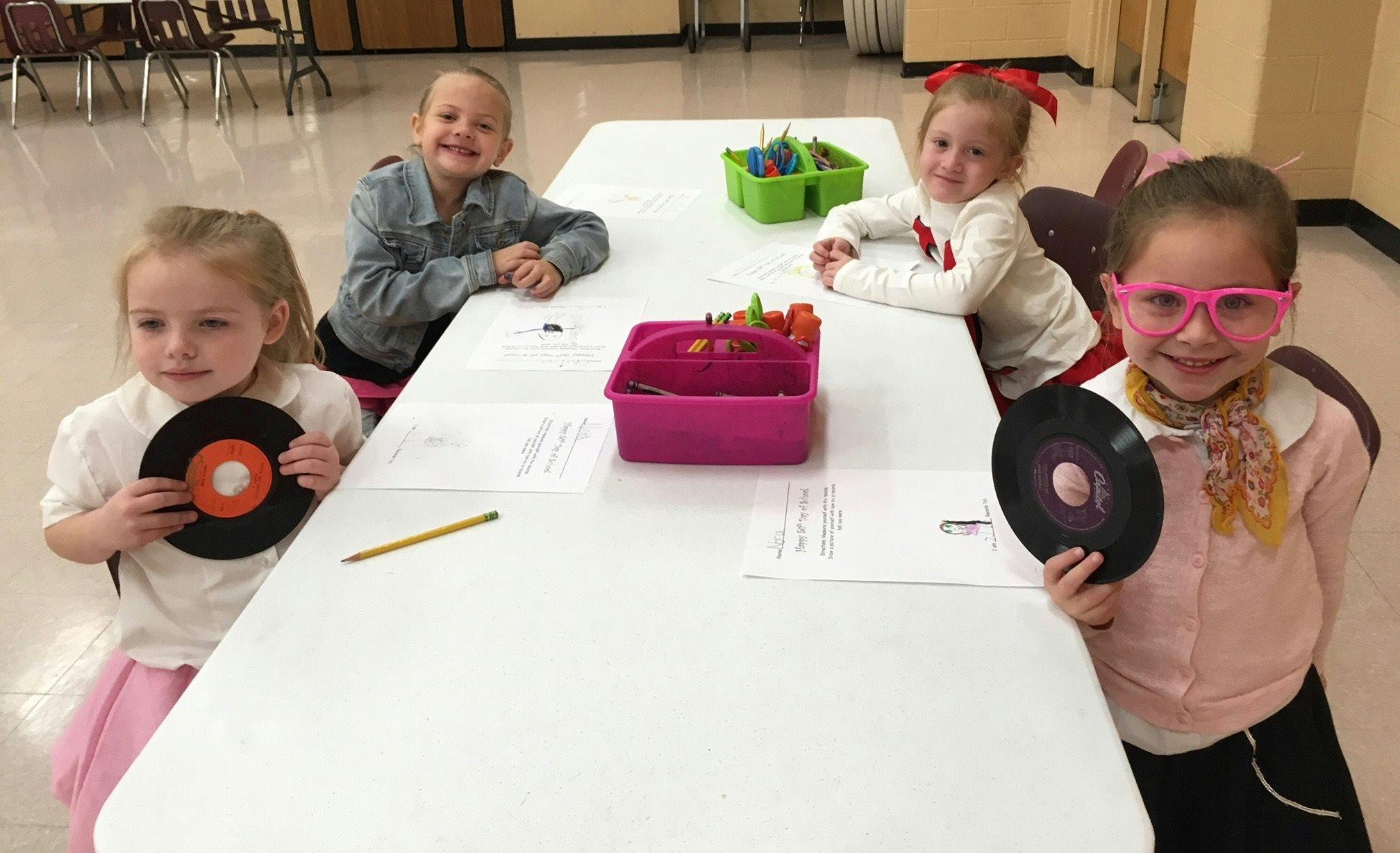 Four children sitting at a table, two holding records