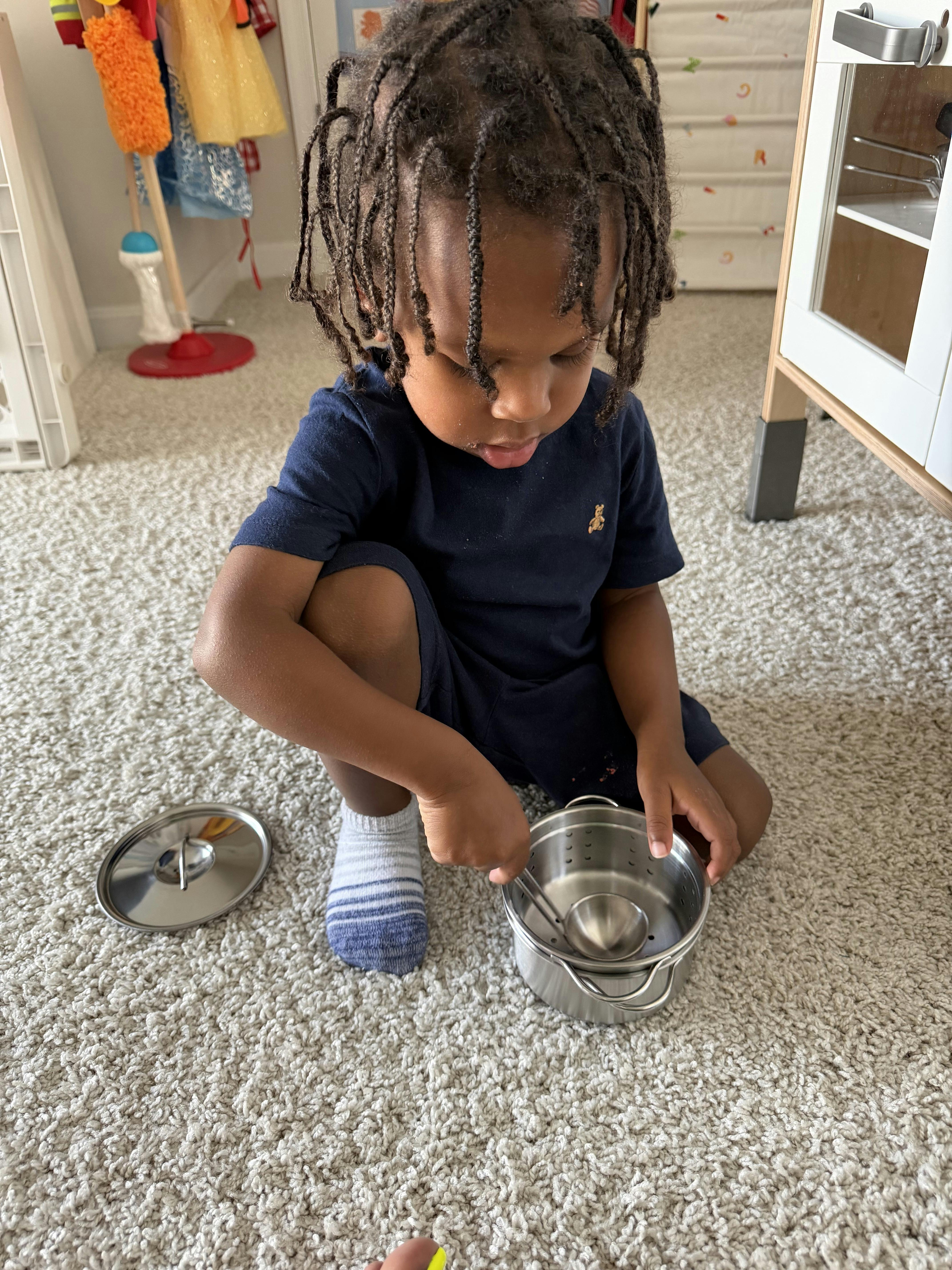 Child playing with metal toy cookware on a carpeted floor