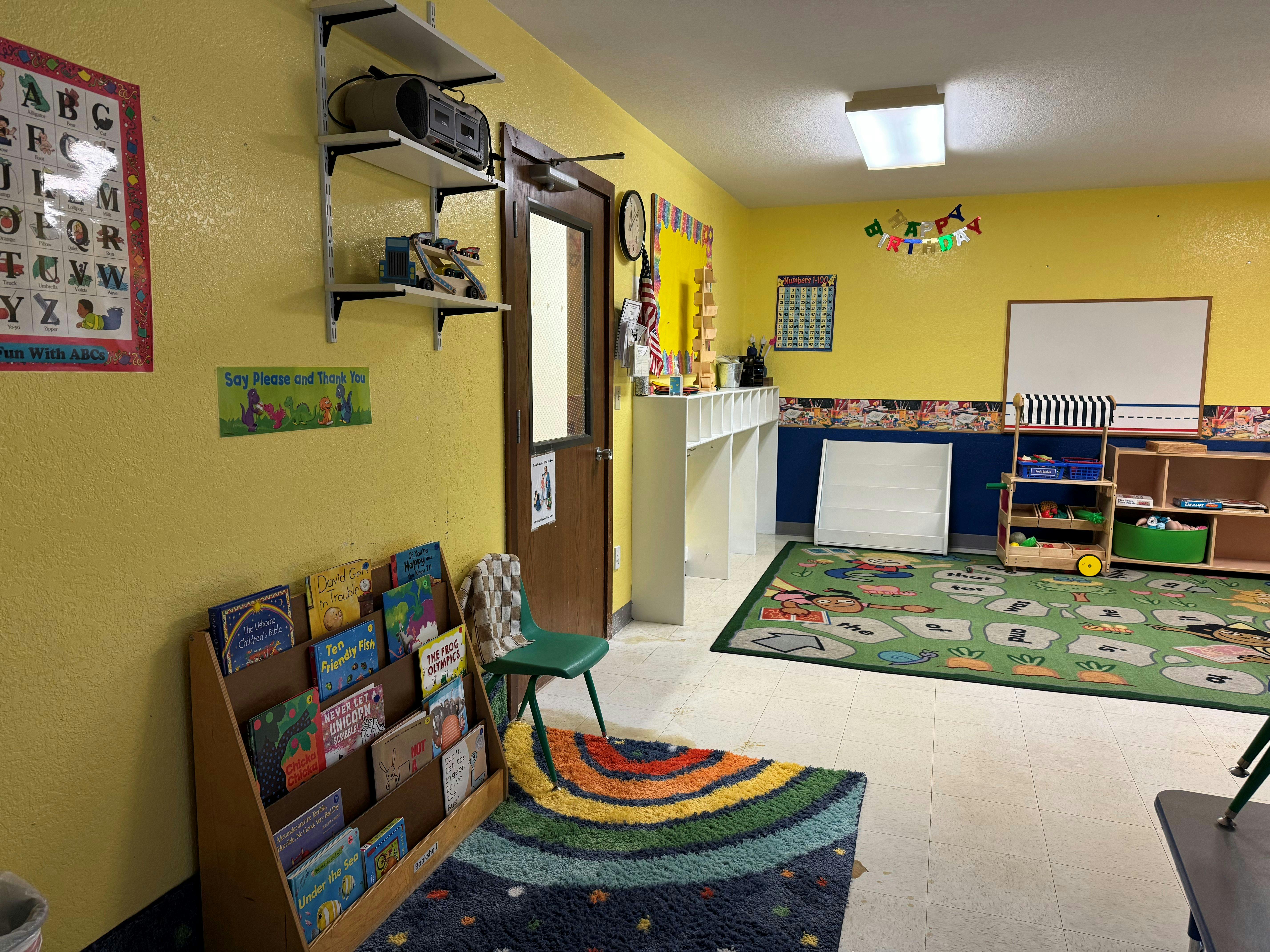 Classroom with yellow walls, children's books, a green rug, and an ABC poster