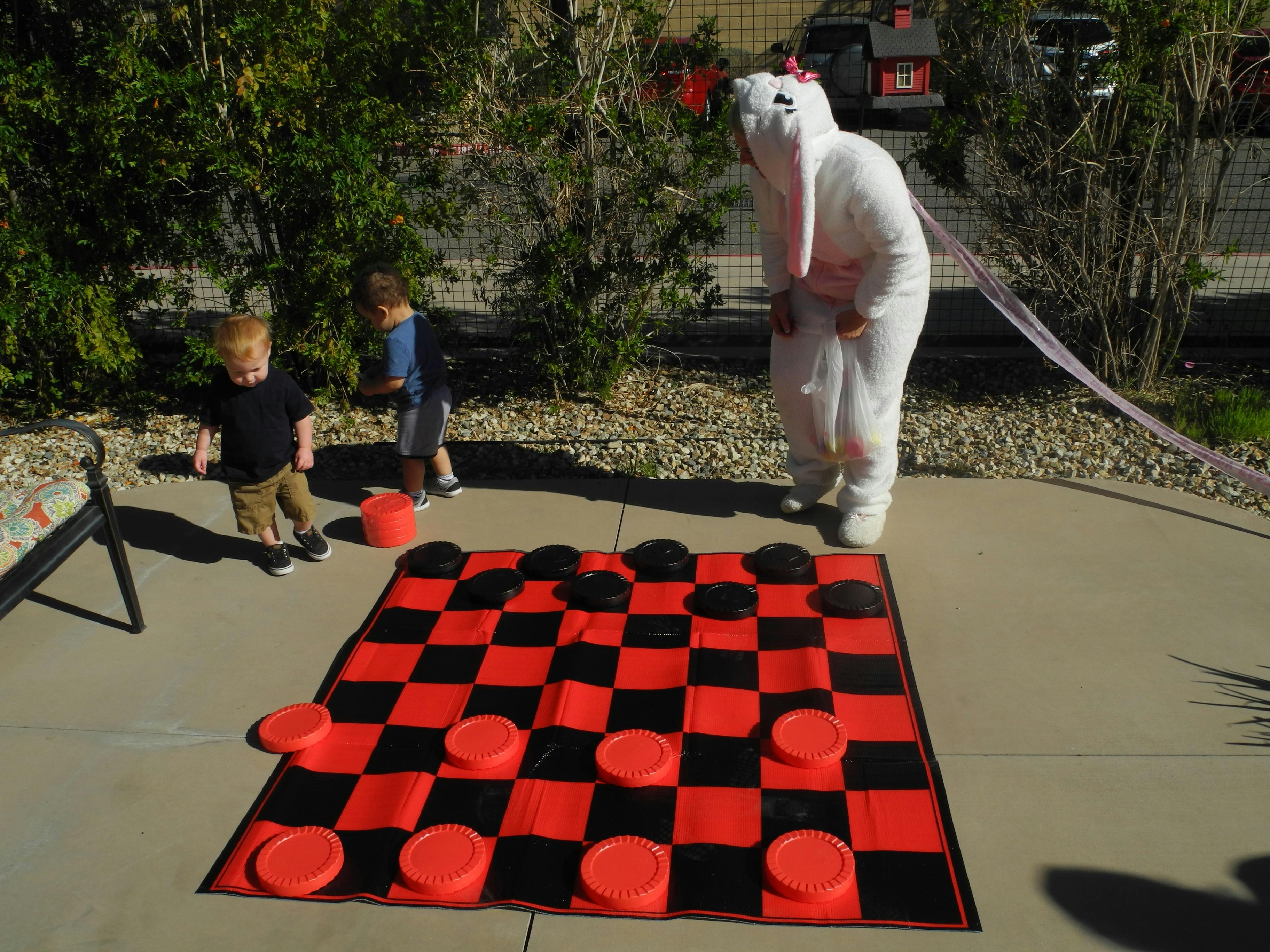 Person in bunny costume with children and a large checkerboard game