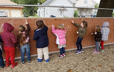 Children drawing on a brown wall outdoors