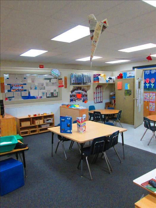 Empty classroom with tables, chairs, and children's artwork on the walls