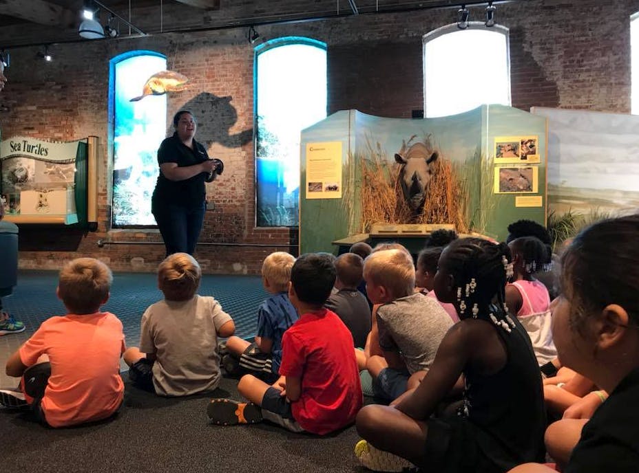 Person speaking to a group of children sitting on the floor in a museum