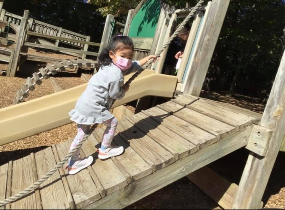 Child in a mask climbing a rope on a wooden playground structure