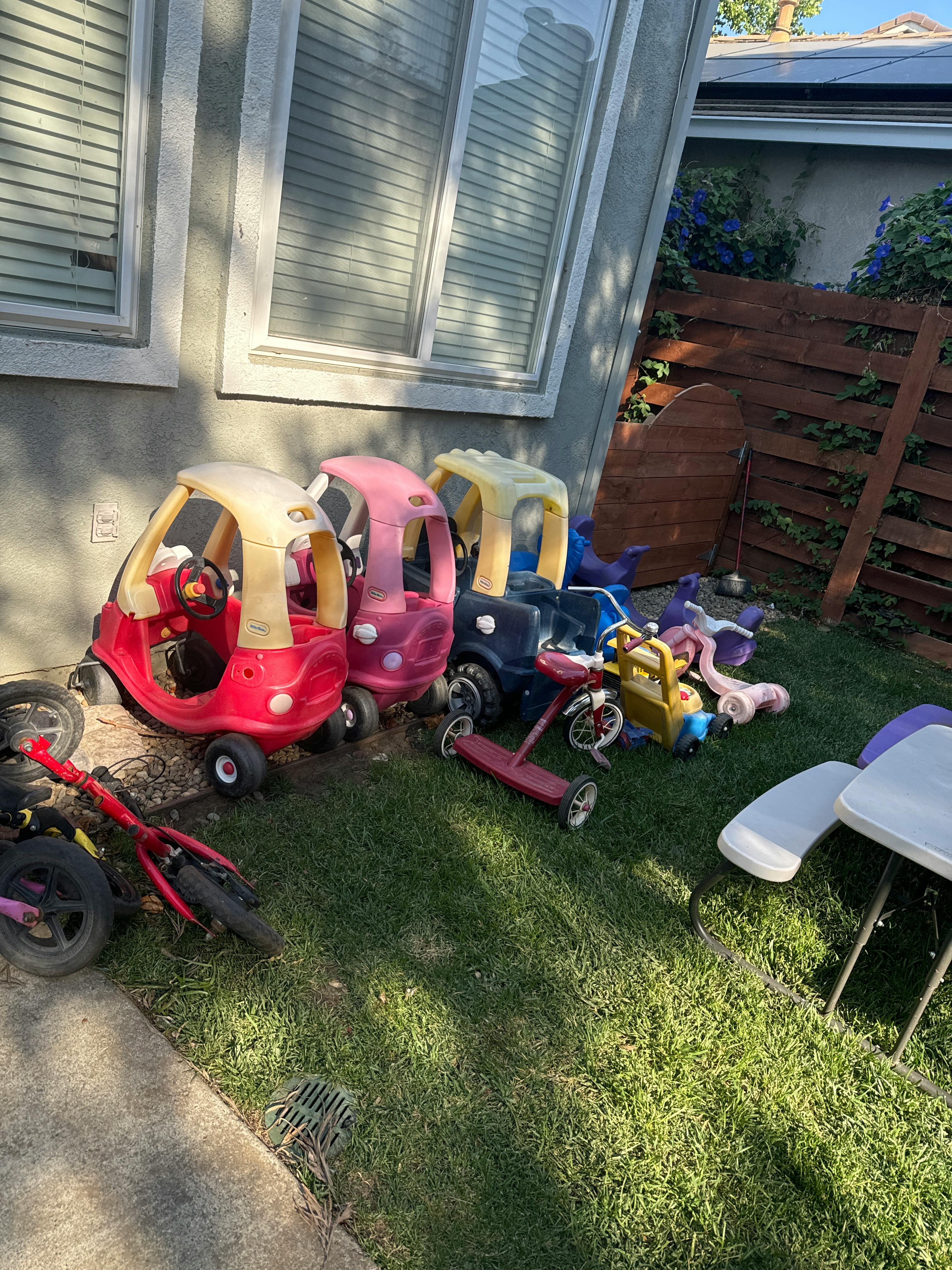 Children's ride-on toys and scooters on grass next to a building