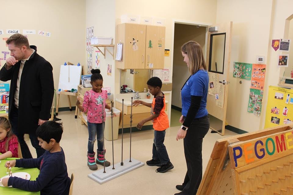Adults and children in a classroom, two children playing with a toy
