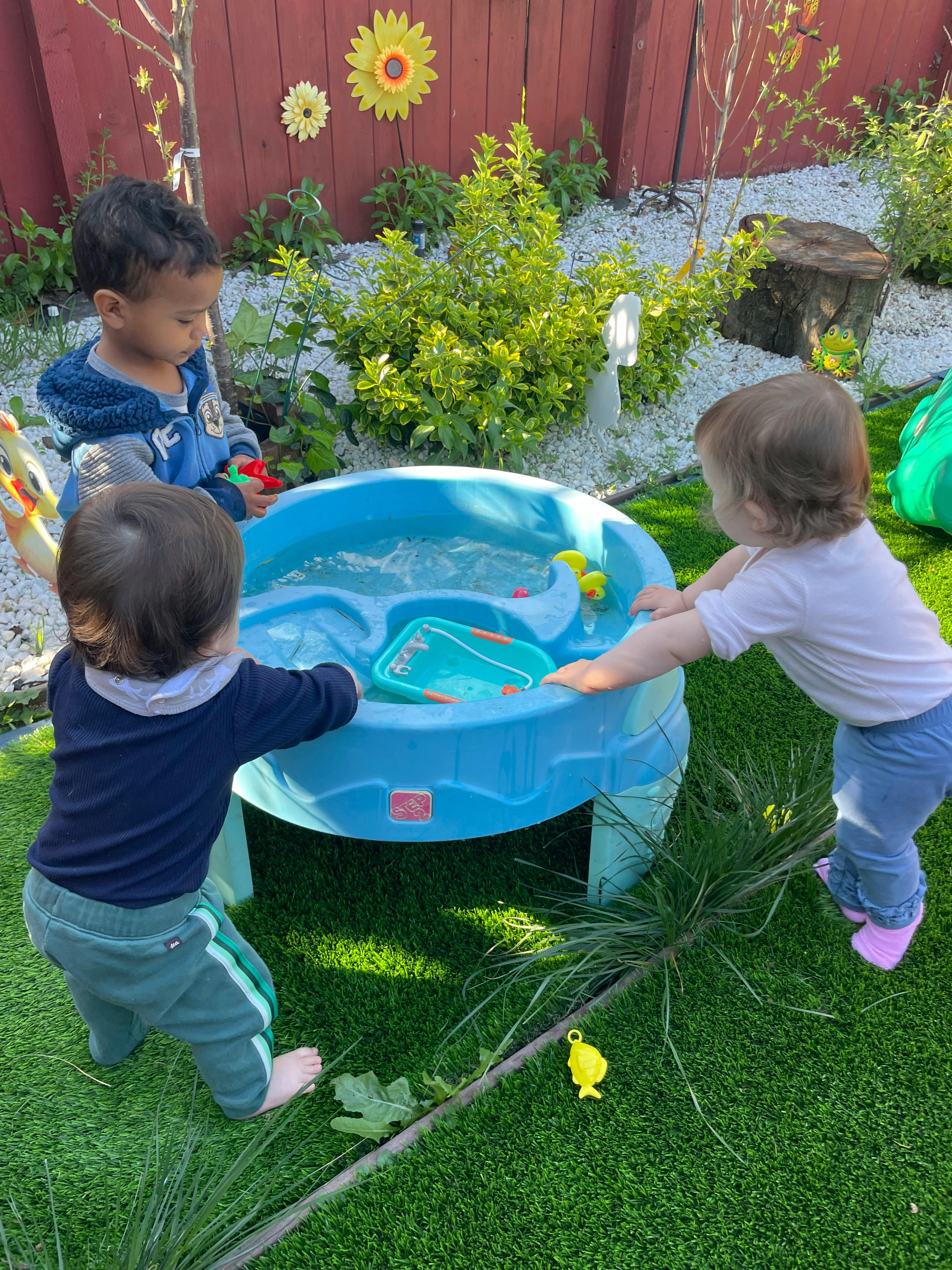 Three children playing around a blue water table outdoors