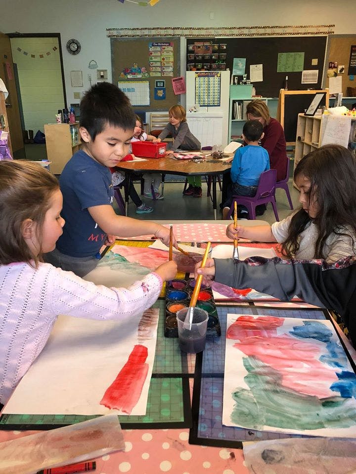 Children painting with watercolors at a table in a classroom