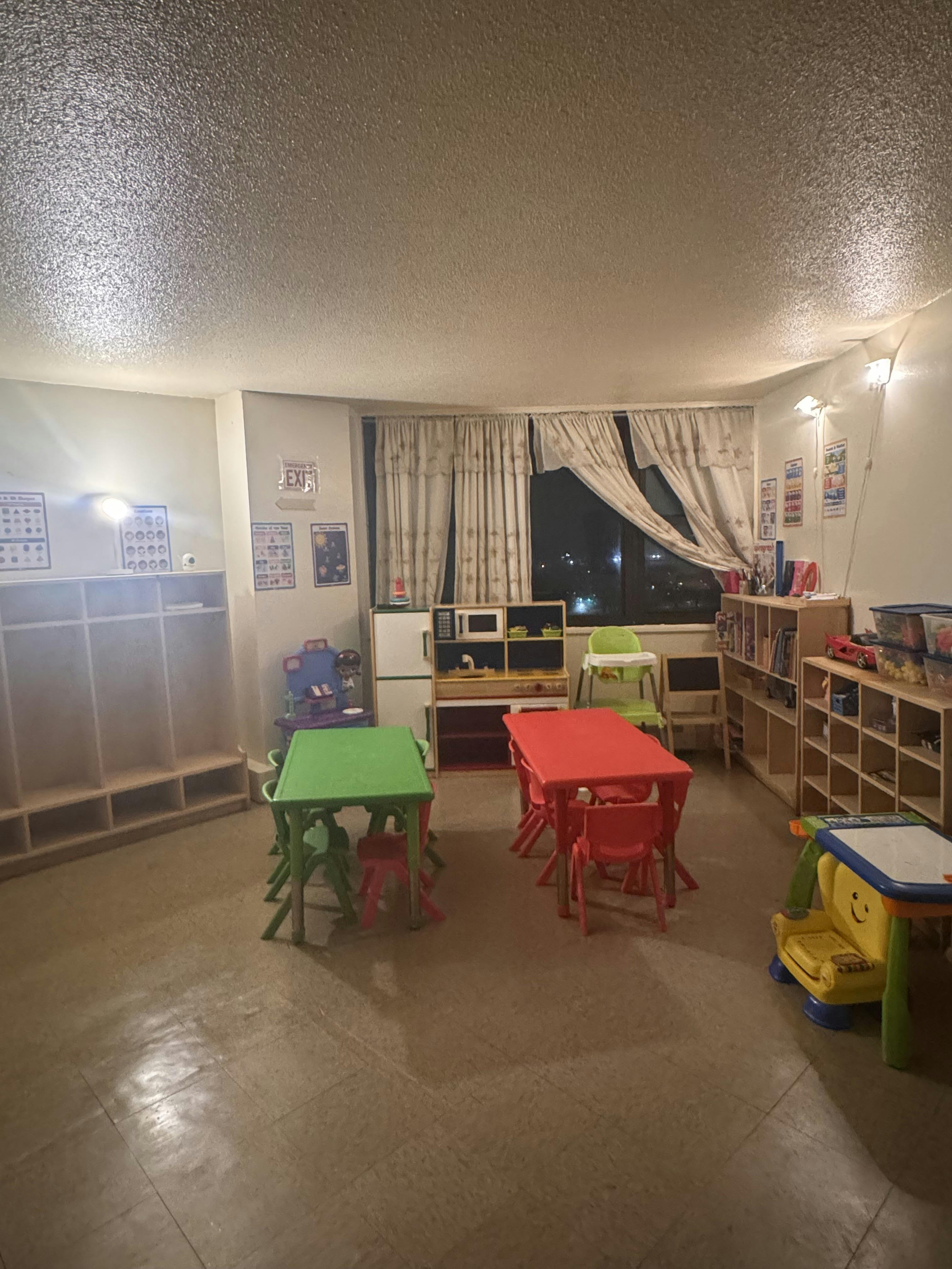Classroom with child-sized tables and chairs, play kitchen, and shelving units
