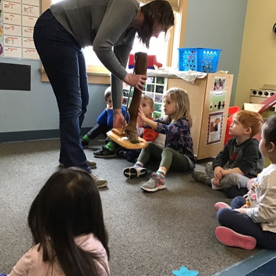Adult and children interacting with a wooden toy in a classroom
