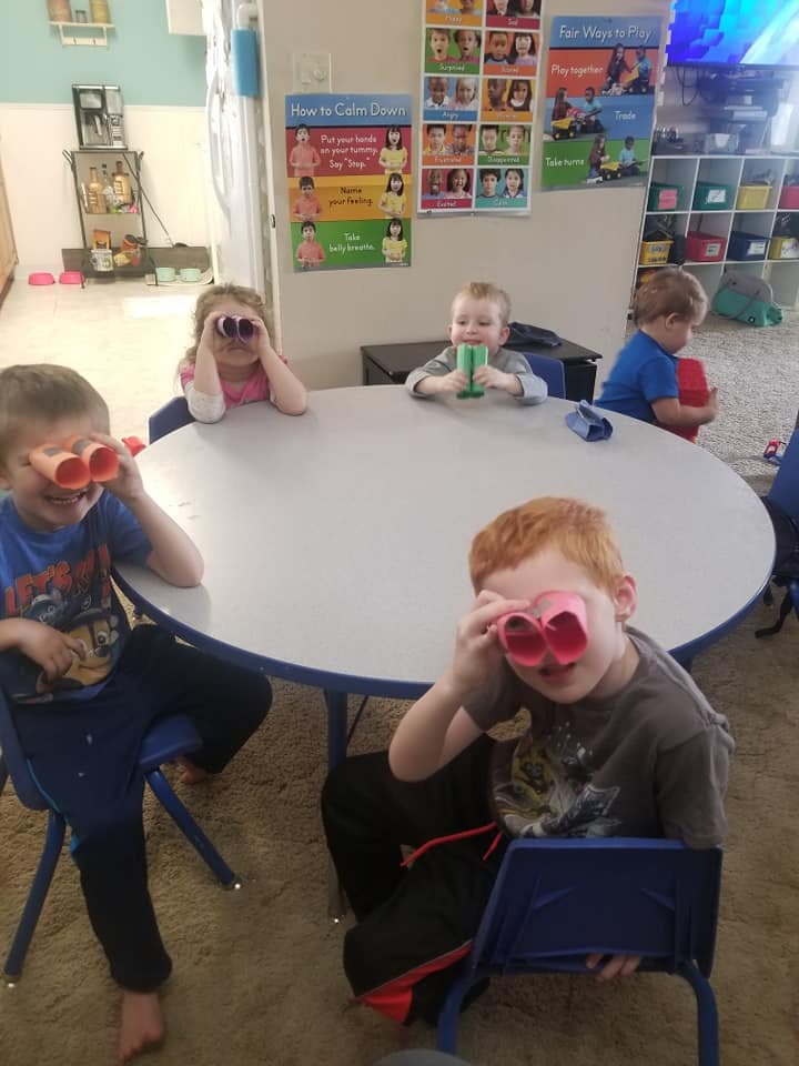 Children sitting at a table, some looking through toy binoculars