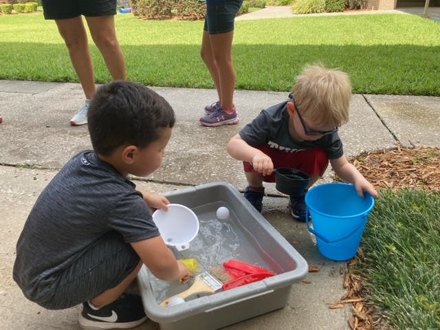 Two children playing with water in a bin and a blue bucket outdoors