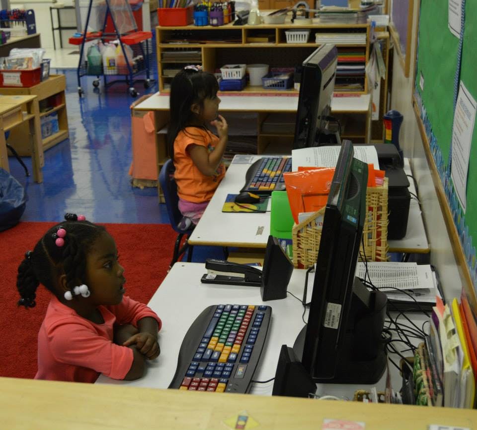 Two children sitting at desks with computers in a classroom