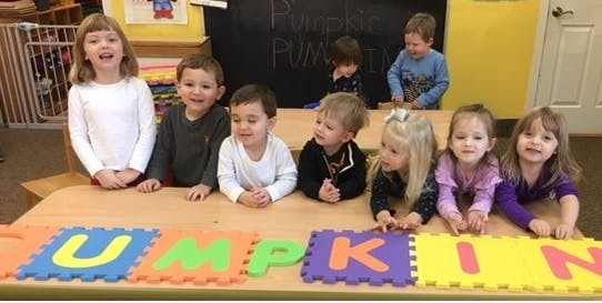 Children sitting at a table with foam letter puzzles spelling "PUMPKIN"