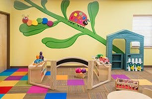 Playroom with colorful floor, playhouse, and wall mural of insects on a branch