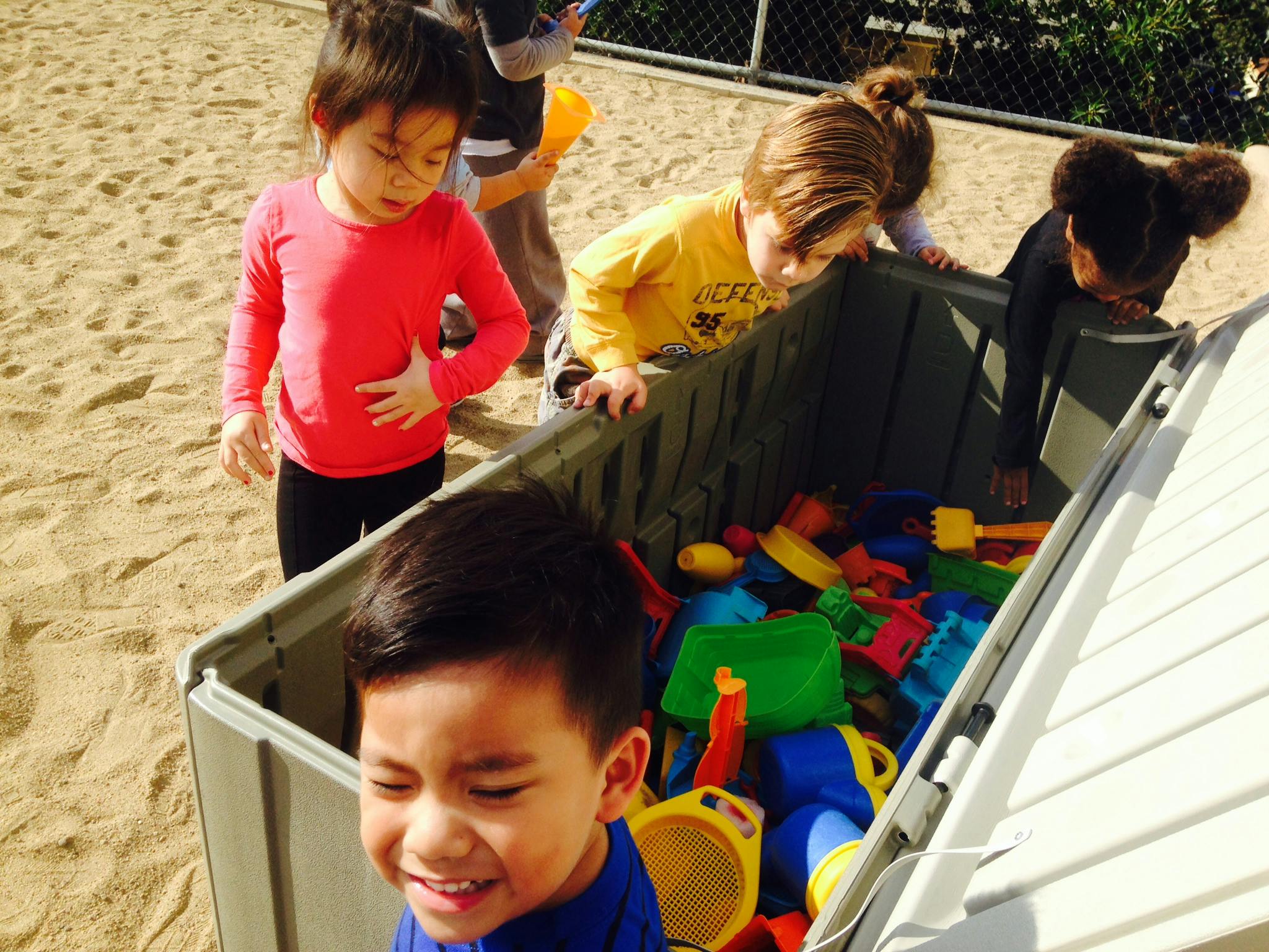 Children looking into a bin of toys in a sandbox
