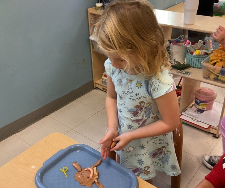 Child playing with clay on a blue tray in a classroom