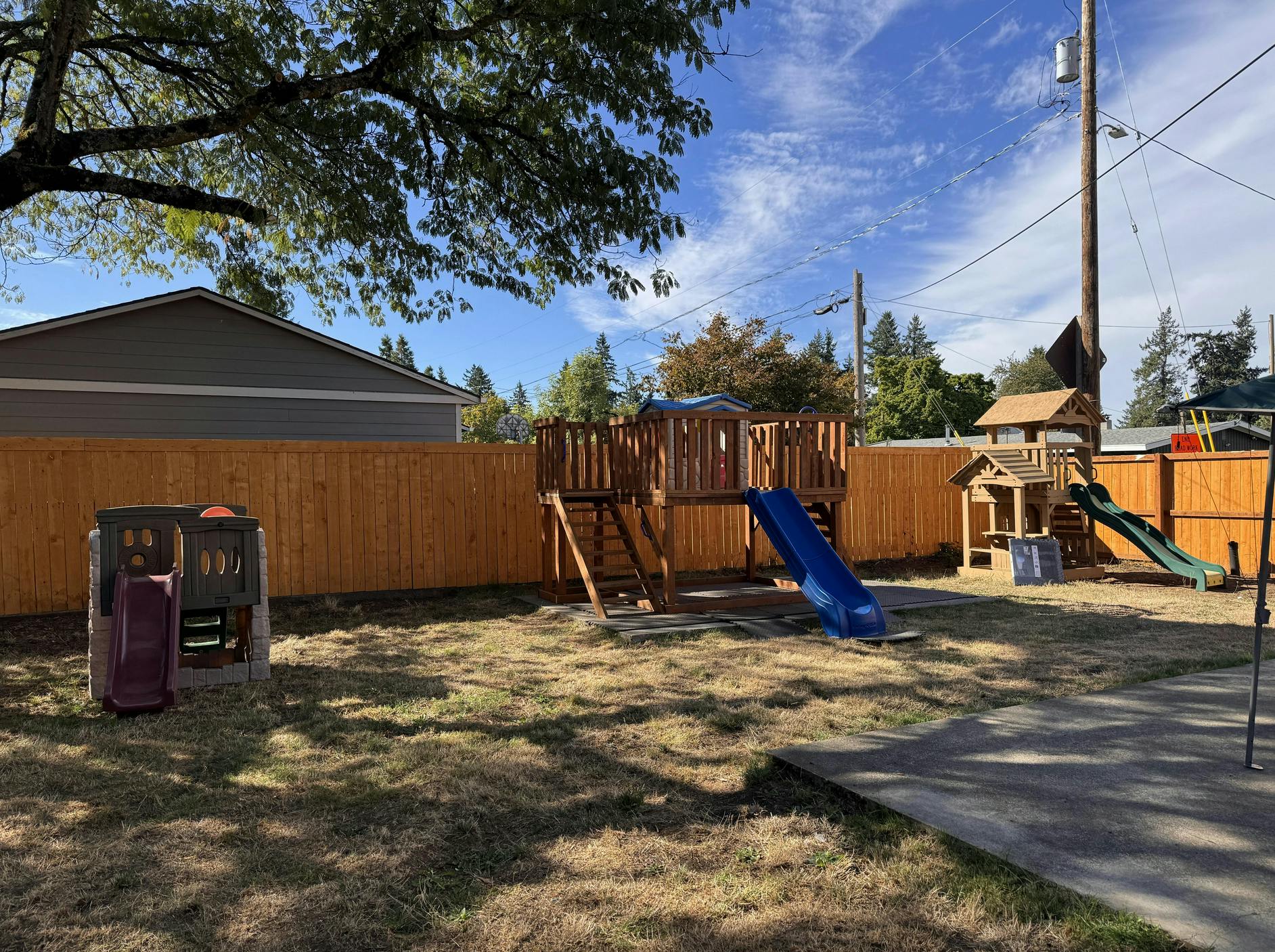 Backyard with wooden playground set, two slides, and a brown fence