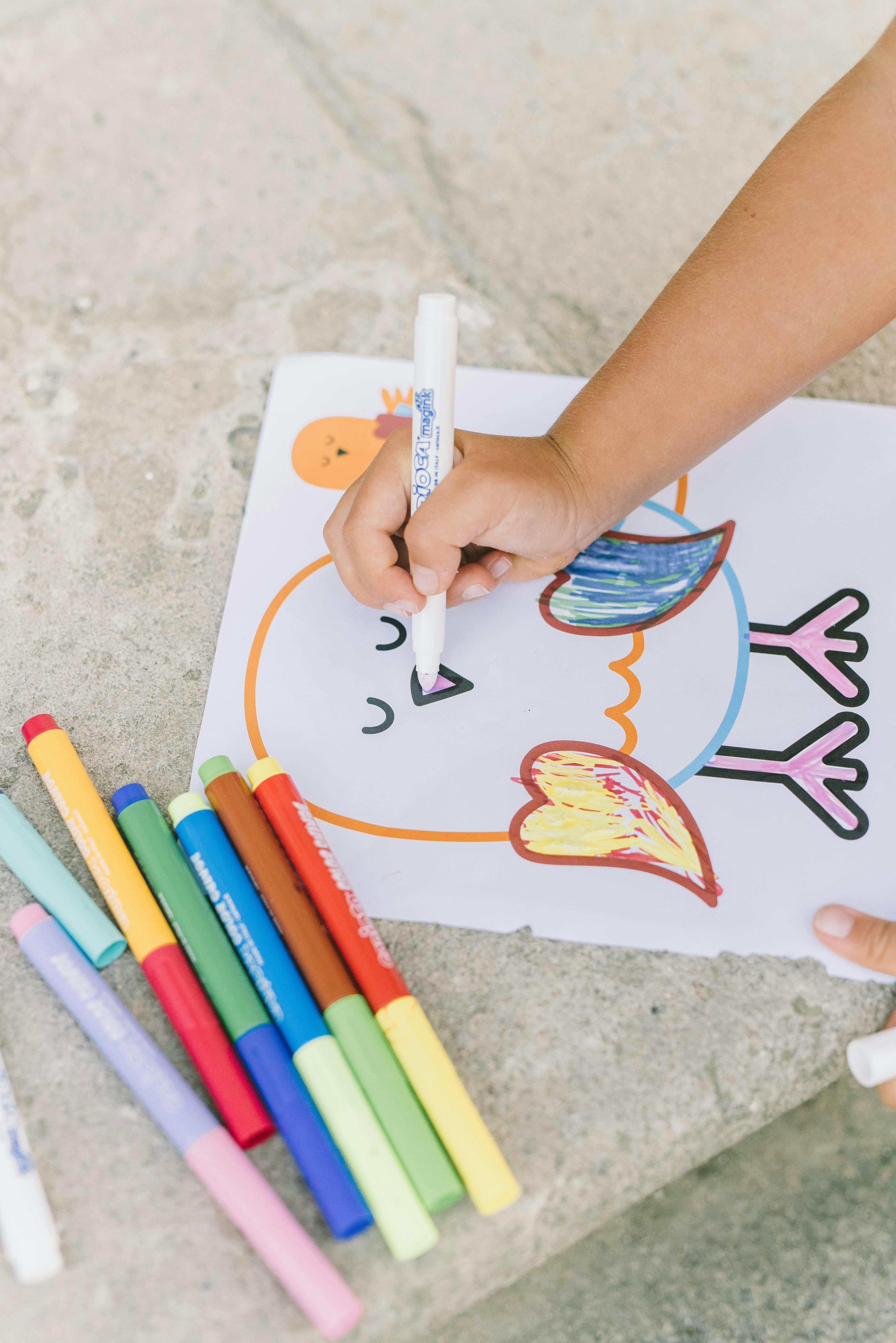 Child's hand coloring a bird drawing with a marker, other markers nearby