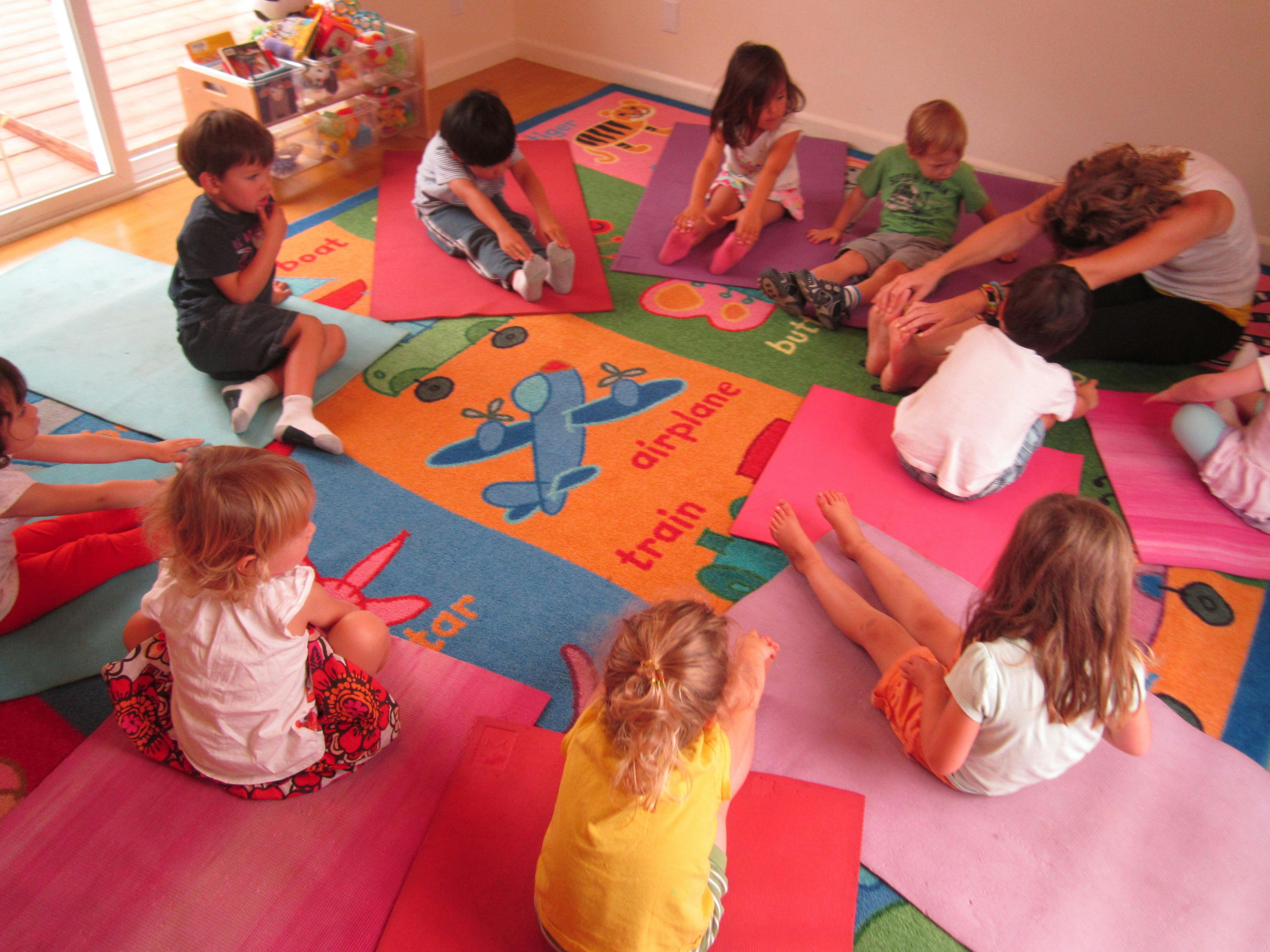 Children and an adult stretching on yoga mats in a classroom