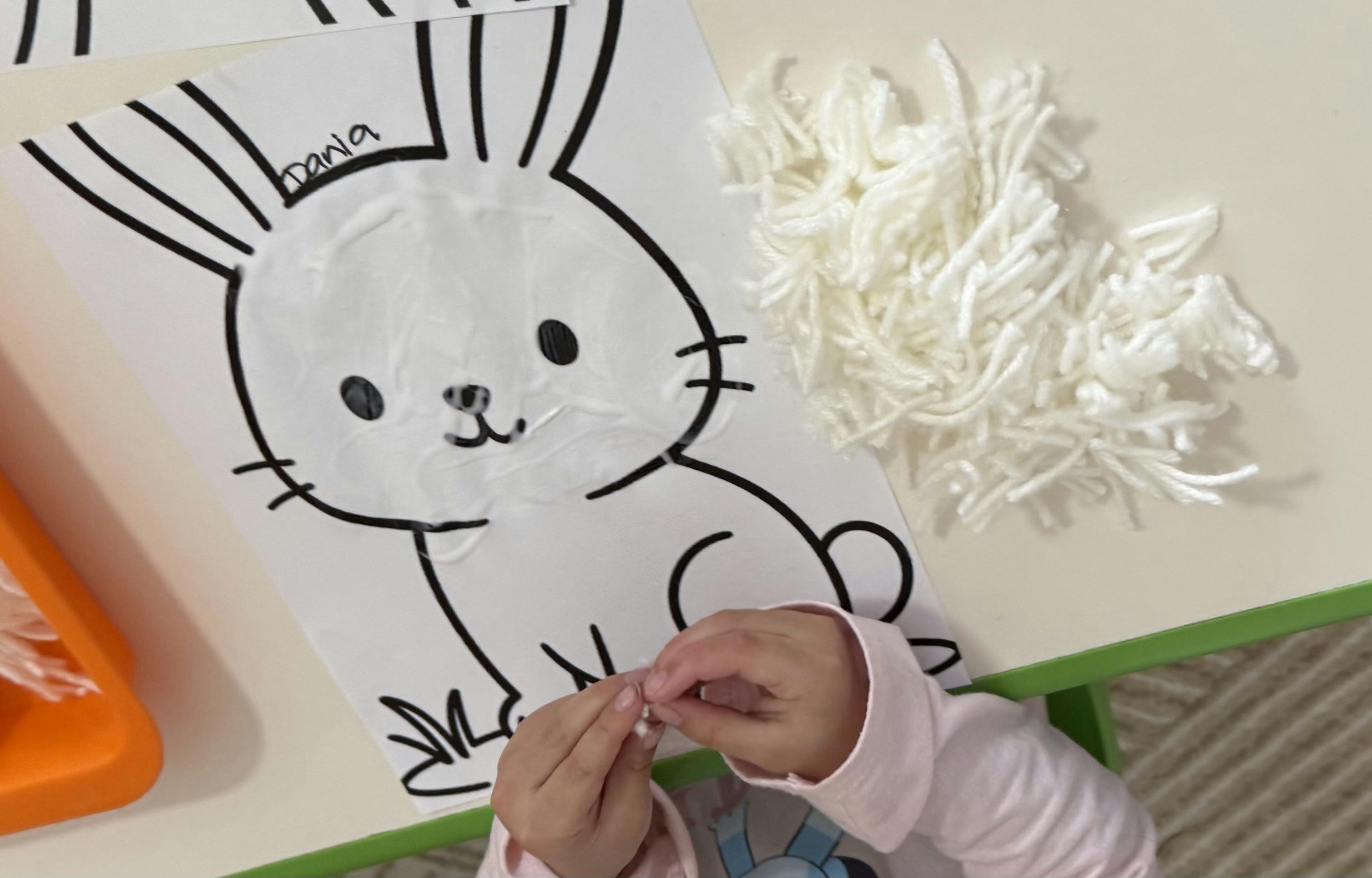 Child applying white yarn to a bunny outline drawing