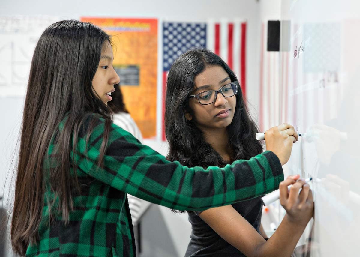 Two teens writing on a whiteboard in a classroom