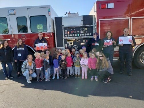 People and children standing in front of two fire trucks