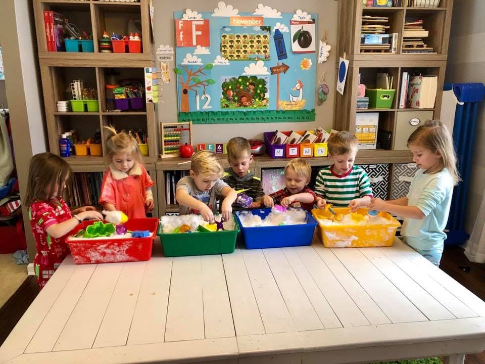 Children playing with sensory bins at a table in a classroom