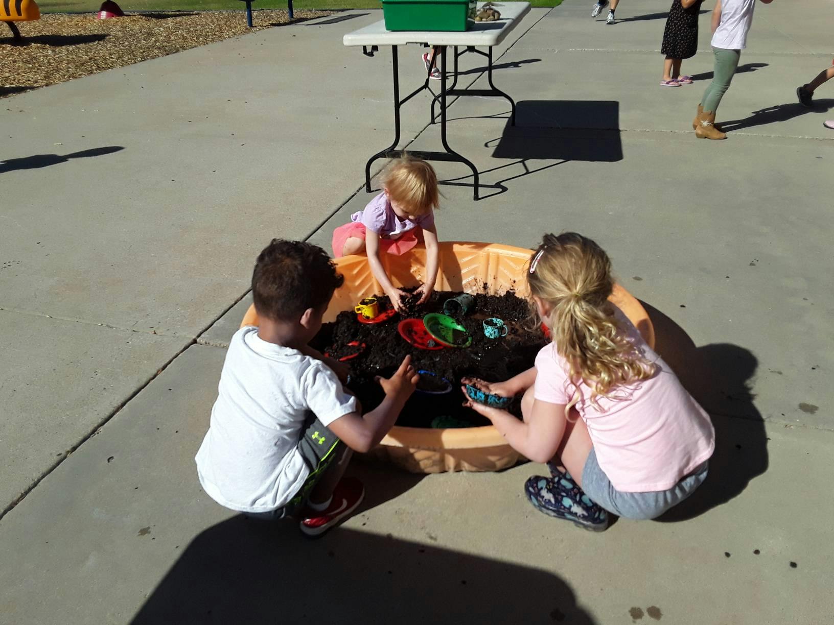 Three children playing with toys in a water table outdoors