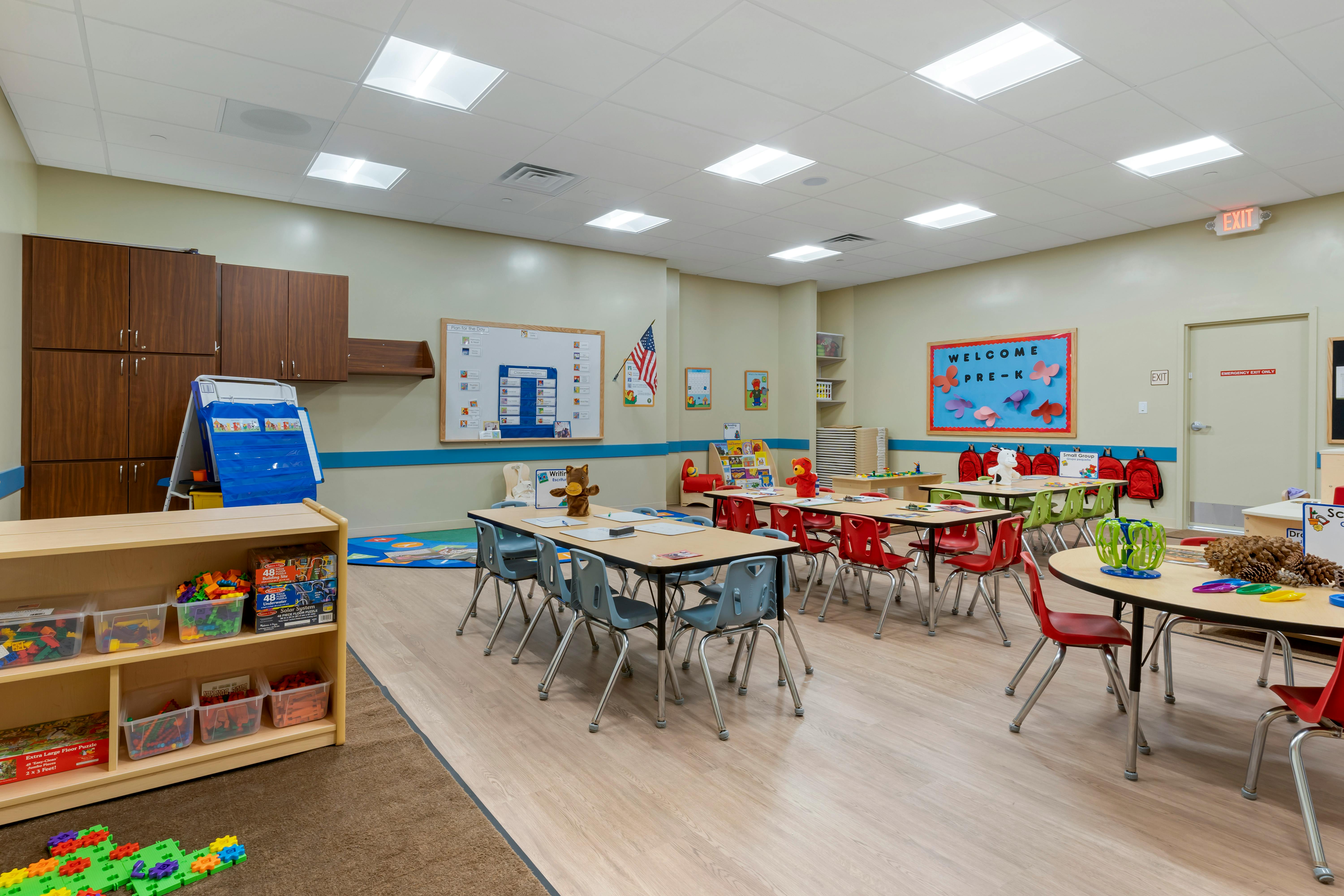 An empty pre-kindergarten classroom with tables, chairs, and learning materials
