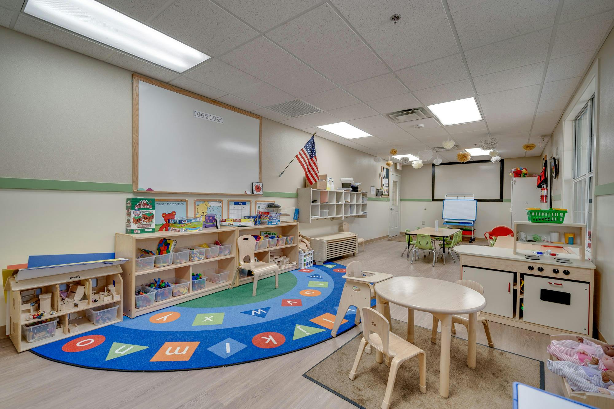 Empty classroom with a colorful rug, shelves, and small tables