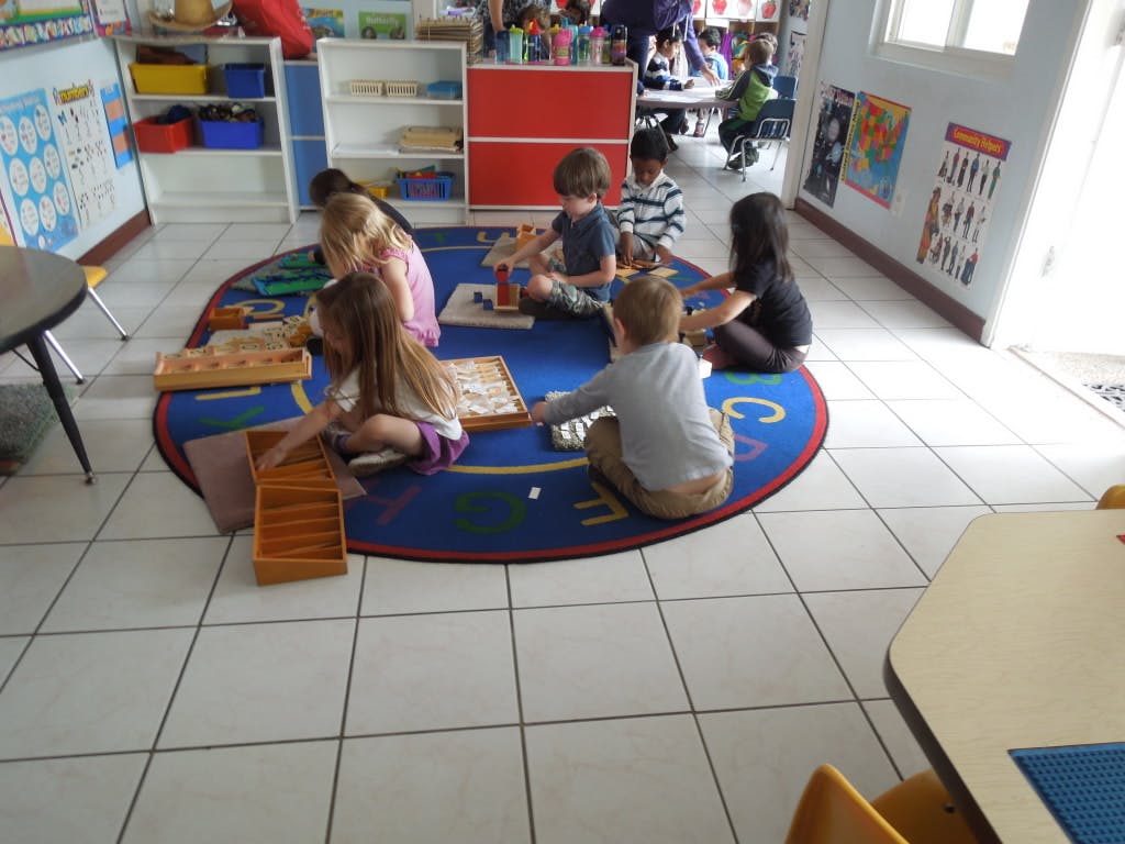 Children sitting on a rug in a classroom playing with toys