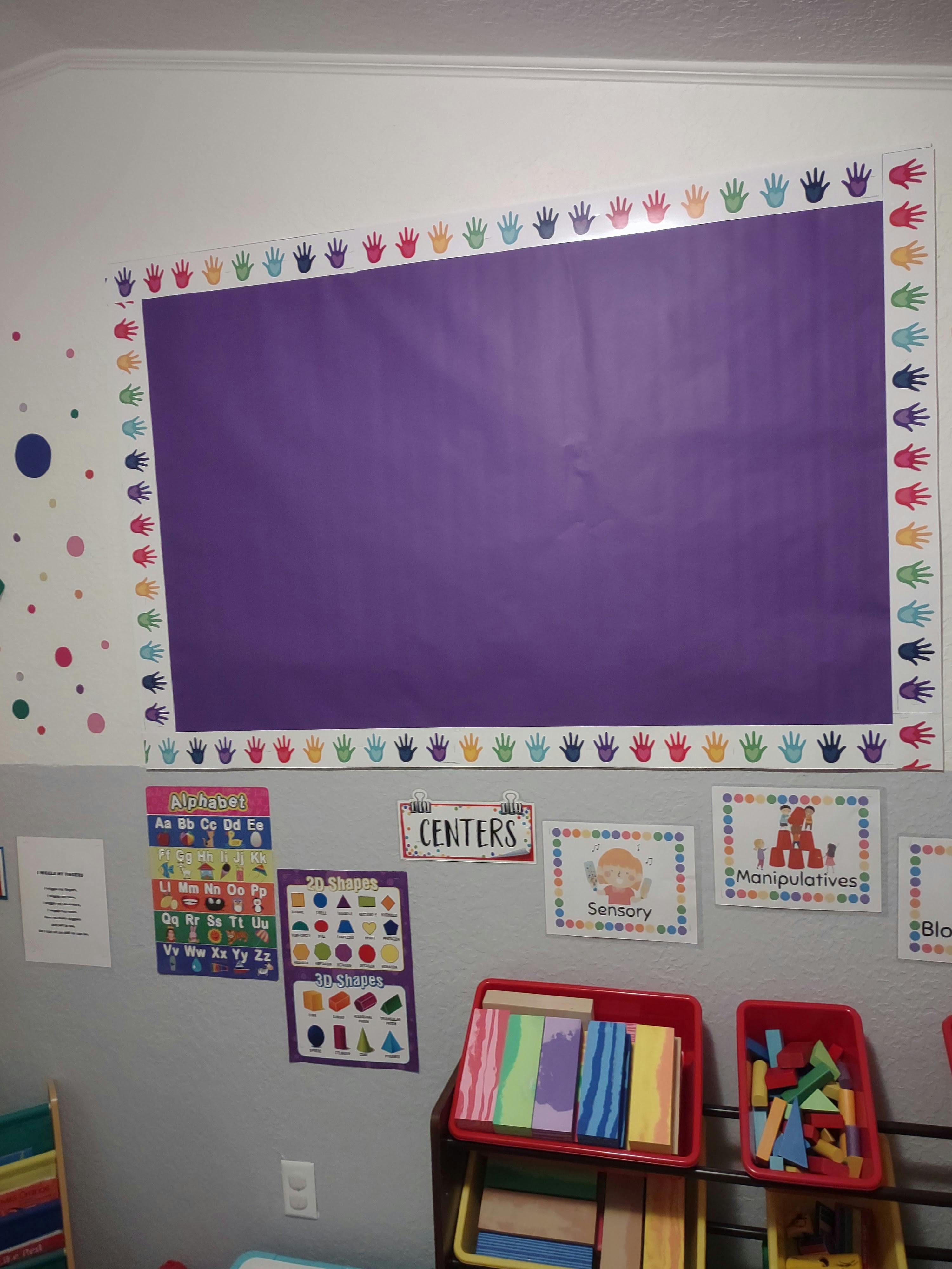 Purple bulletin board with colorful handprint border in a classroom