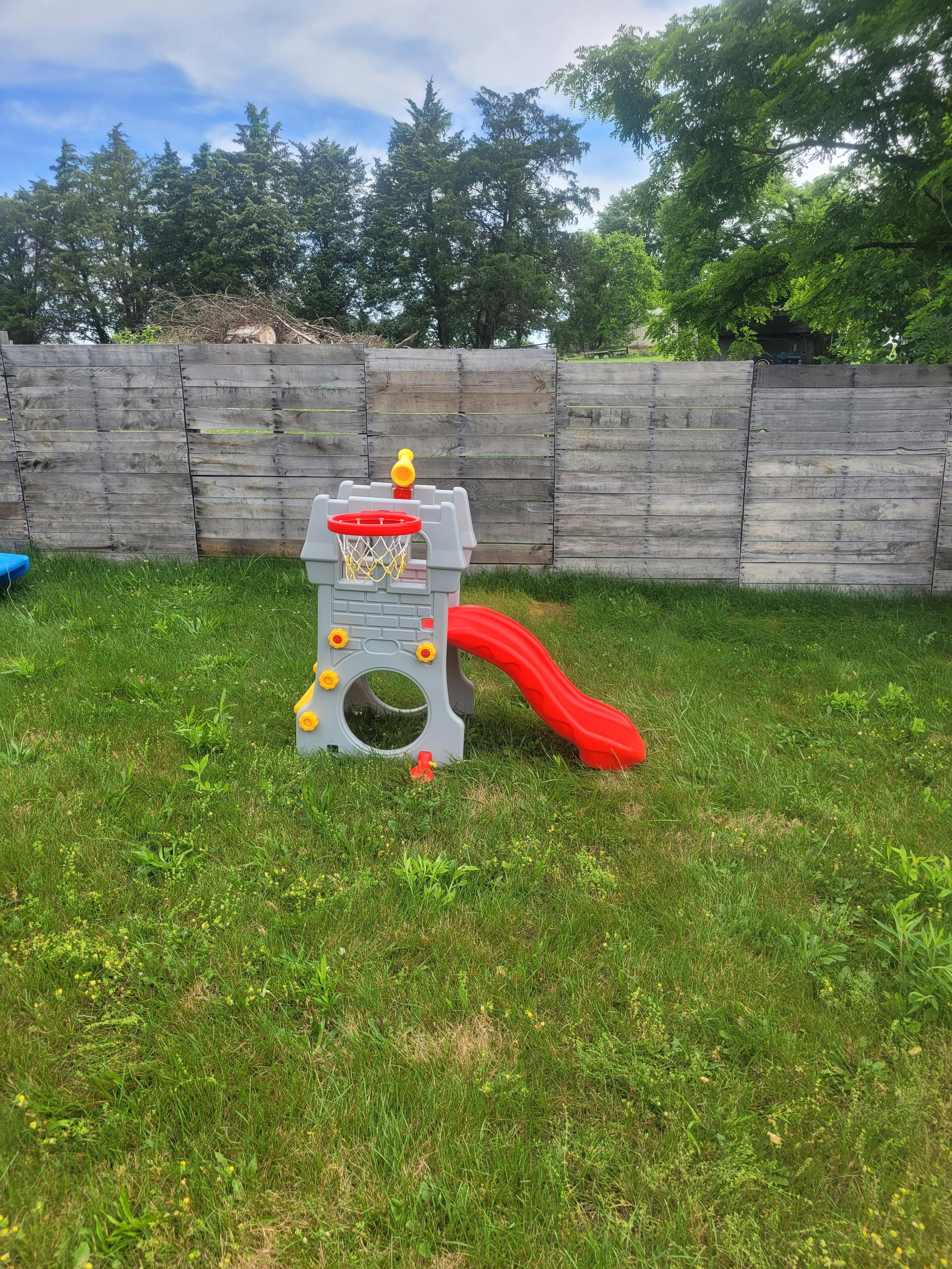 Plastic toy playground structure with a slide and basketball hoop in a yard