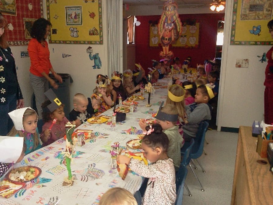 Children sitting at a long table with a person standing nearby