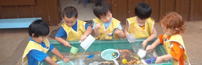 Five children playing with water and toys in a trough