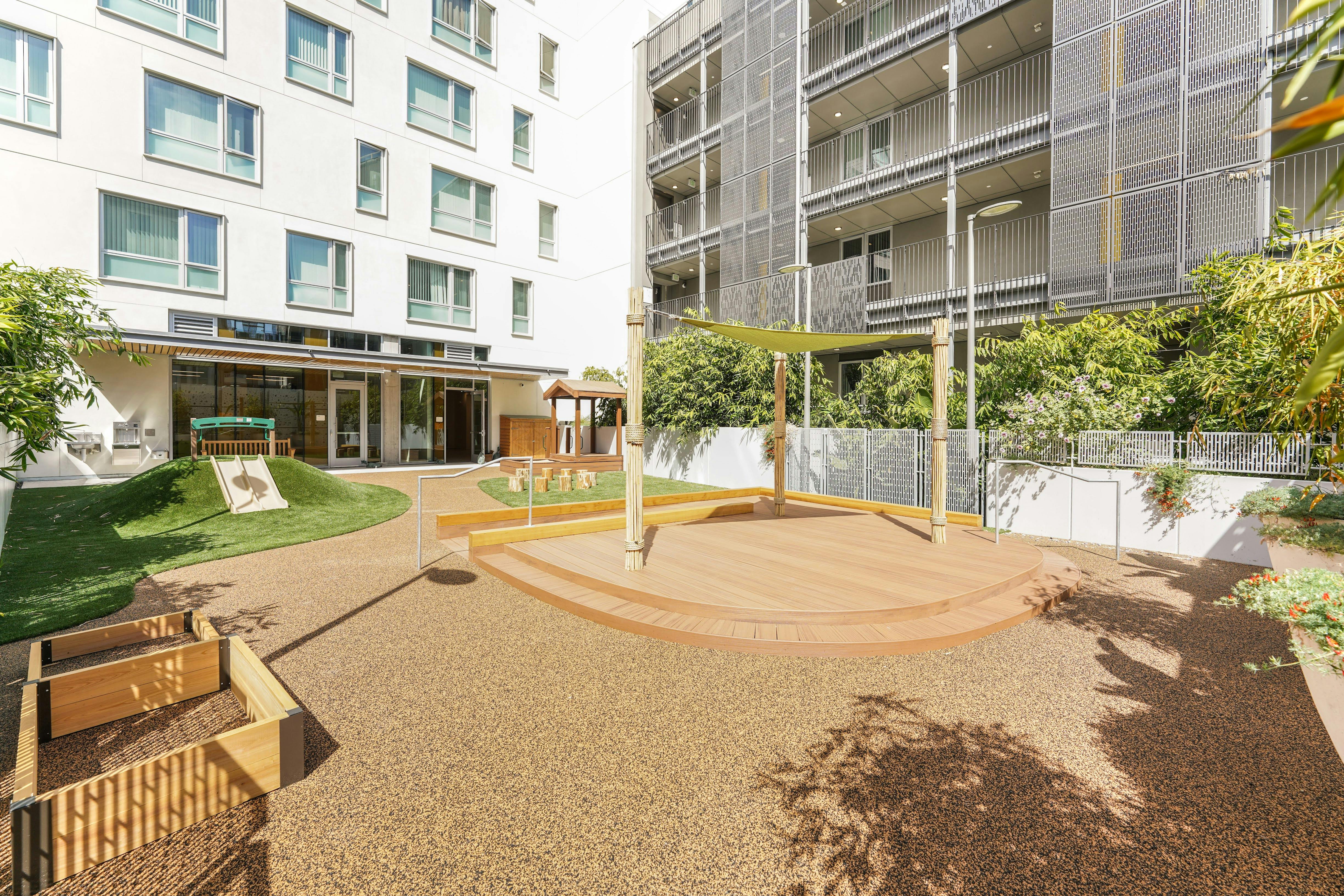 Playground area with a small slide and raised wooden deck in an urban courtyard